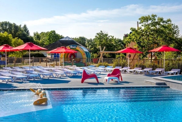 A swimming pool with lounge chairs and umbrellas, surrounded by trees and a playground.
