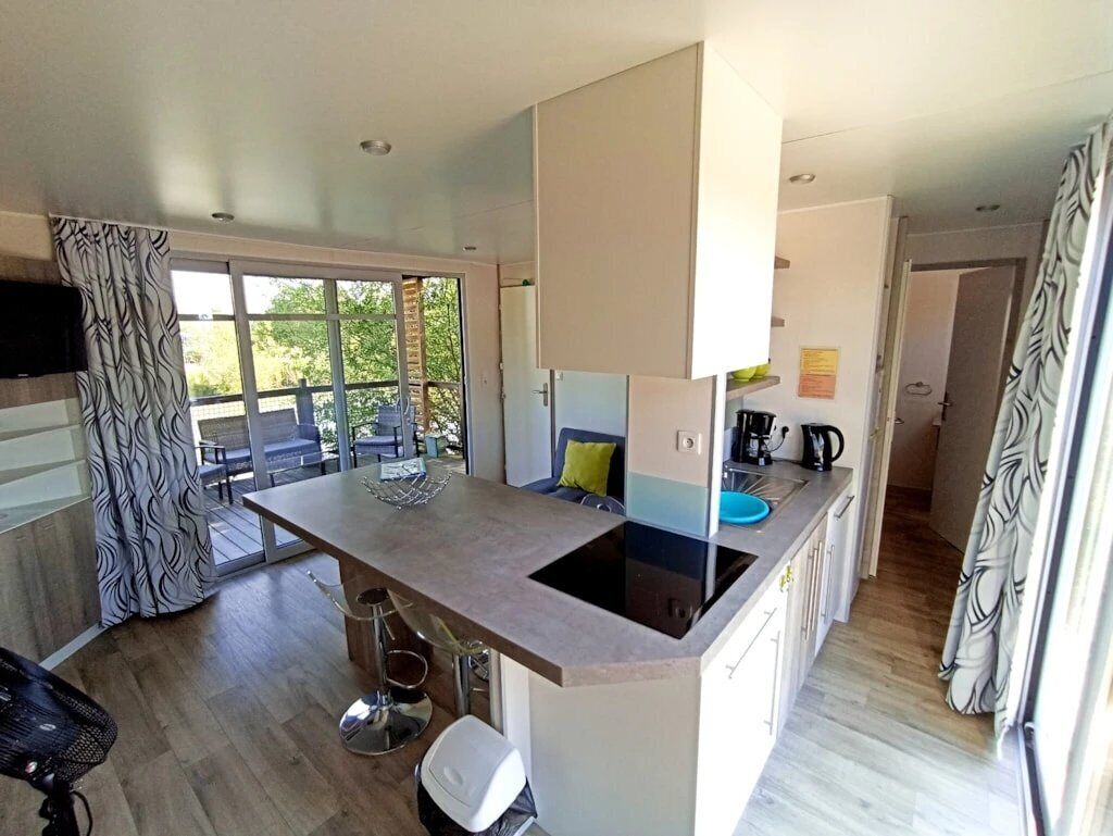 A modern kitchen with a central island, a dining area with a table and chairs, and a view of the outdoors through large windows.