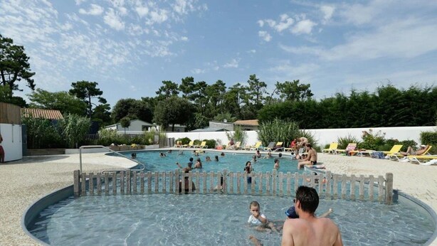 Un área de piscina con varias piscinas, rodeada de sillas de descanso y una zona de arena.