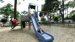 Un parque infantil con tobogán, estructuras de escalada y una zona de arena.