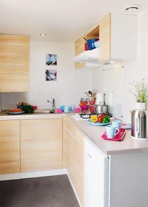 Una cocina moderna con armarios de madera, un hervidor de acero inoxidable y una variedad de utensilios de cocina coloridos.