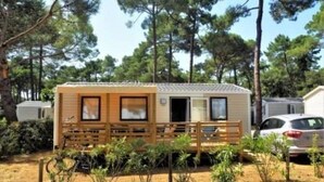 Ein Wohnmobil mit einer Holzterrasse und einem eingezäunten Garten, umgeben von Bäumen.