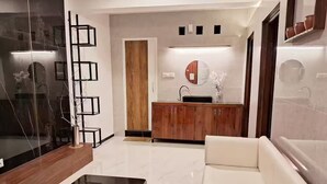Een moderne woonkamer met een witte bank, een houten salontafel en een keukenhoek met een houten kastje en een ronde spiegel boven de wasbak.
