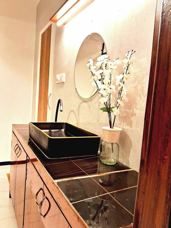 Une salle de bain avec un lavabo noir, un miroir et un vase contenant des fleurs blanches.