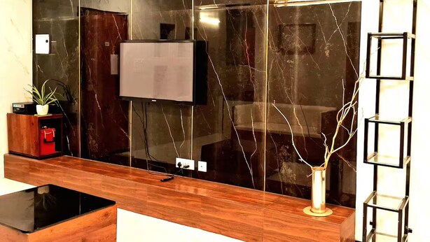 Een moderne woonkamer met een grote zwarte marmeren wand, een flatscreen televisie, een houten salontafel en een decoratieve vaas.