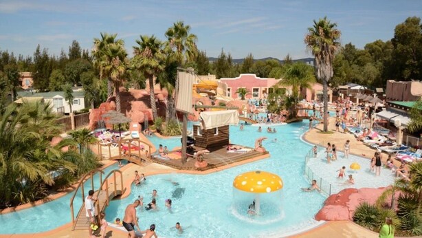 A large outdoor swimming pool with multiple water features and palm trees.