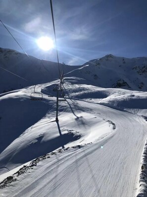Uma cadeira de teleférico desliza por um caminho nevado na montanha sob um céu claro e ensolarado.