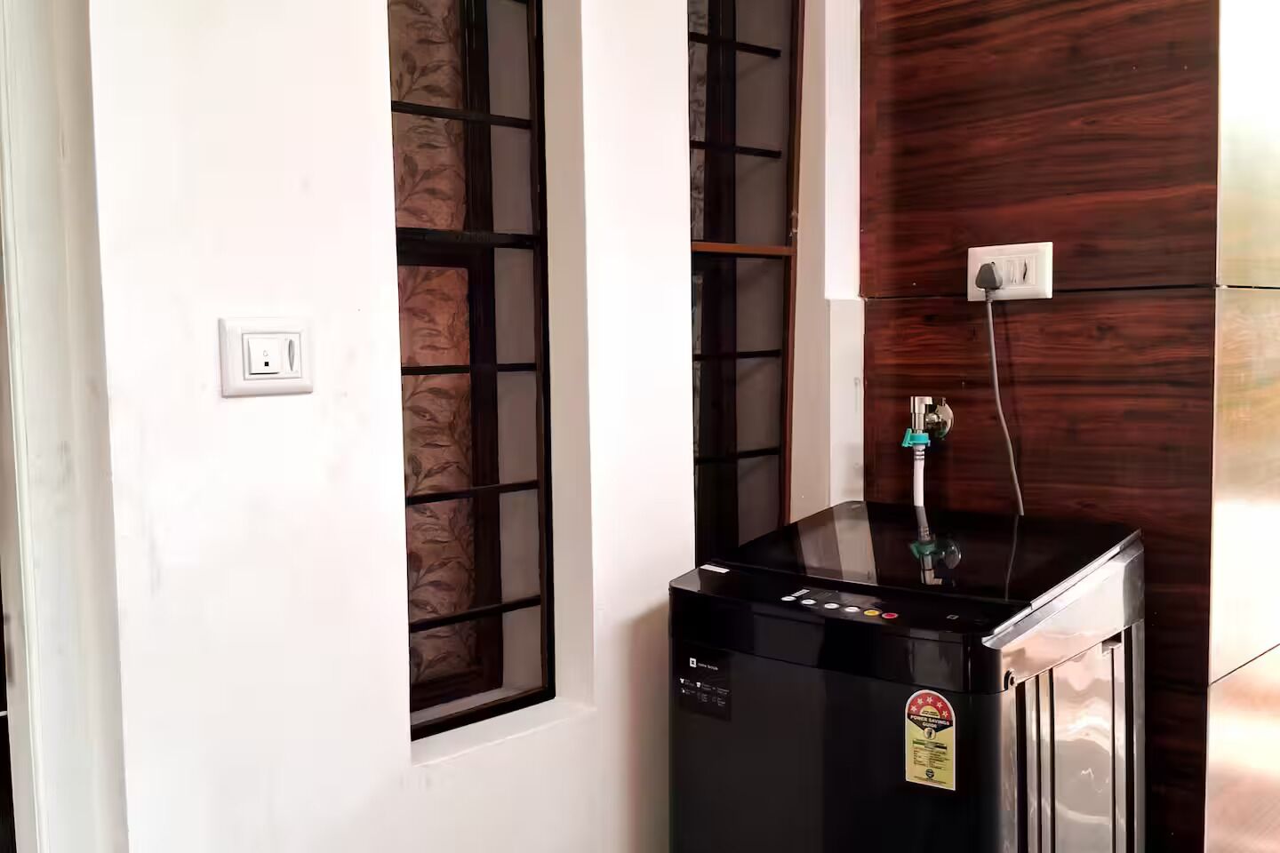 A compact room with a water dispenser, a window with a decorative screen, and a wall with a wooden panel.