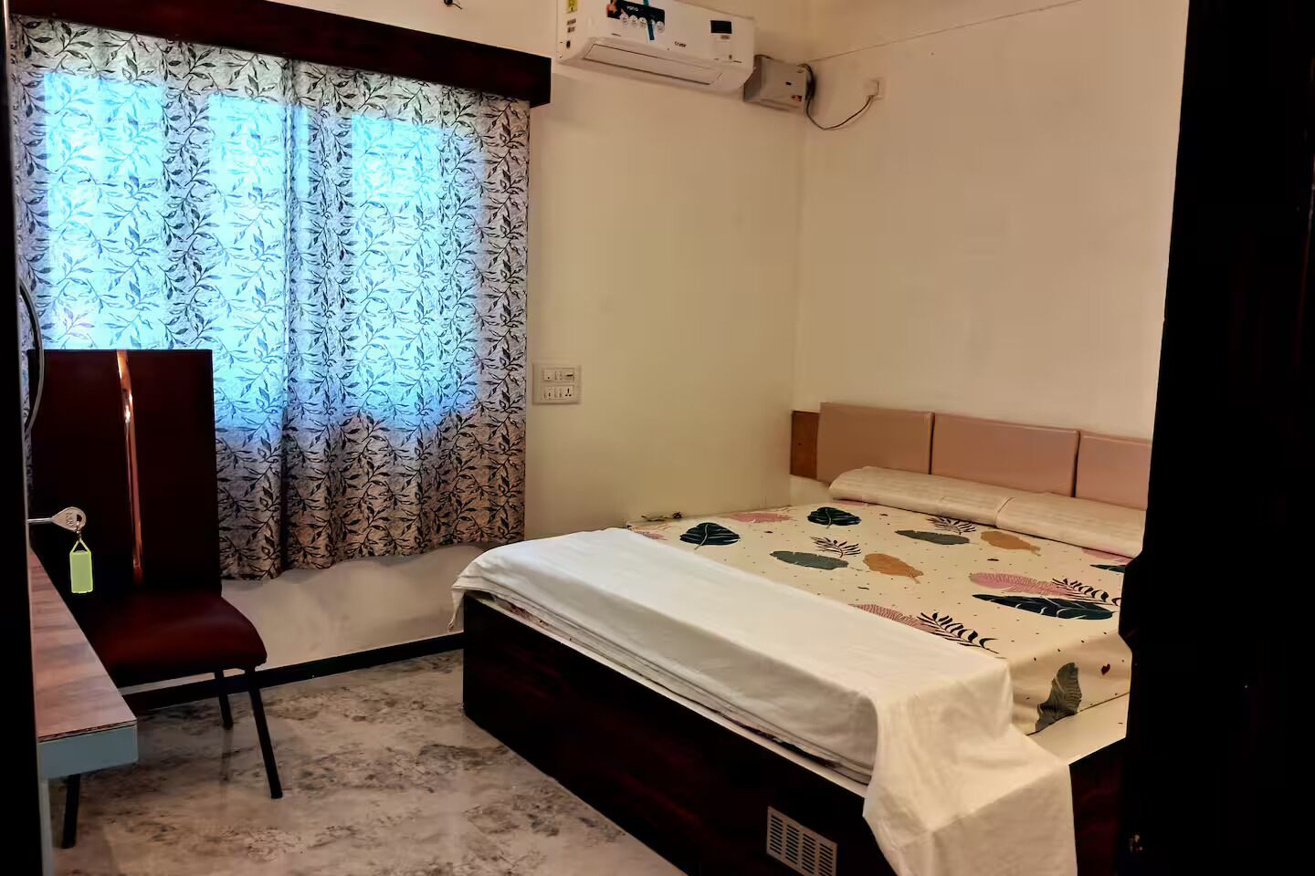 Une chambre à coucher avec un lit, un bureau, une chaise et une fenêtre ornée de rideaux à motifs.