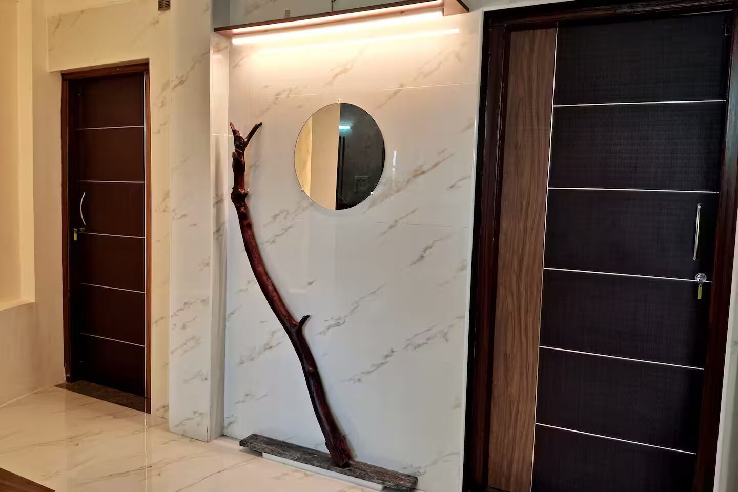 Een hal met een marmeren vloer, een houten deur met een spiegel en een houten kast met planken.