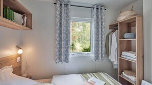 Une chambre à coucher comprenant un lit, une fenêtre avec des rideaux, une table de chevet, une étagère avec des objets décoratifs et une armoire.