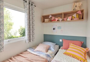 Un dormitorio con cama, ventana con cortinas, estante con adornos y pared con calendario y una pequeña imagen de un animal.