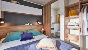 Une chambre à coucher moderne, avec un lit, des tables de chevet, une armoire et une salle de bain visible à travers une porte ouverte.