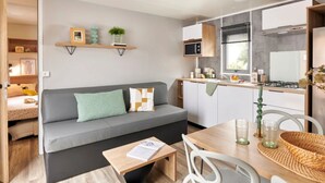 A compact living space with a sofa, a dining table, and a kitchenette. - ZEcamping 3 étoiles pet friendly locatif TV LV clim 6 pers (Pouzauges)