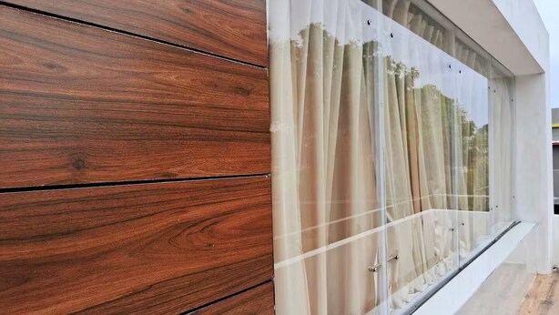 Ein modernes Gebäude mit Holzverkleidung und großen Fenstern mit transparenten Vorhängen.