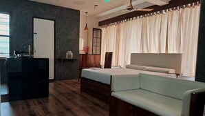 Ein modernes Hotelzimmer mit Holzboden, einem Bett, einer Couch, einem Schreibtisch mit Spiegel und einem Fenster mit Vorhängen.