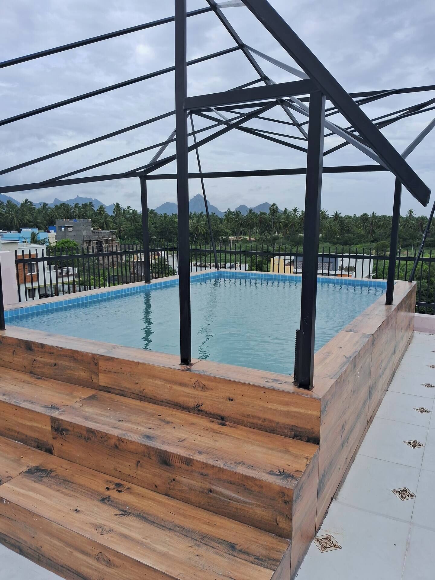 A rooftop swimming pool with a wooden deck and metal railing, surrounded by a metal structure.