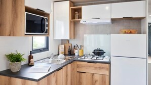 A modern kitchen with wooden cabinets, a built-in microwave, a gas stove, and a refrigerator. - ZEcamping 3 étoiles chiens acceptés locatif TV 6 pers (Pouzauges)