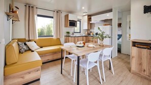 A modern kitchen with white cabinets, a wooden dining table, and a yellow sofa. - ZEcamping 3 étoiles chiens acceptés locatif TV 6 pers (Pouzauges)