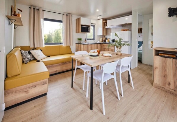 A modern kitchen with white cabinets, a wooden dining table, and a yellow sofa. - ZEcamping 3 étoiles chiens acceptés locatif TV 6 pers (Pouzauges)