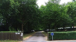 A gated entrance with a blue sign, a wooden fence, and lush green trees. - ZEcamping 3 étoiles chiens acceptés locatif TV 6 pers (Pouzauges)