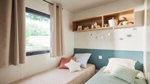 A small, cozy room with two single beds, a window with curtains, and a shelf with various items. - ZEcamping 3 étoiles chiens acceptés locatif TV 6 pers (Pouzauges)