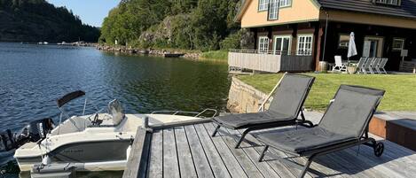 A wooden dock with two lounge chairs and a boat.