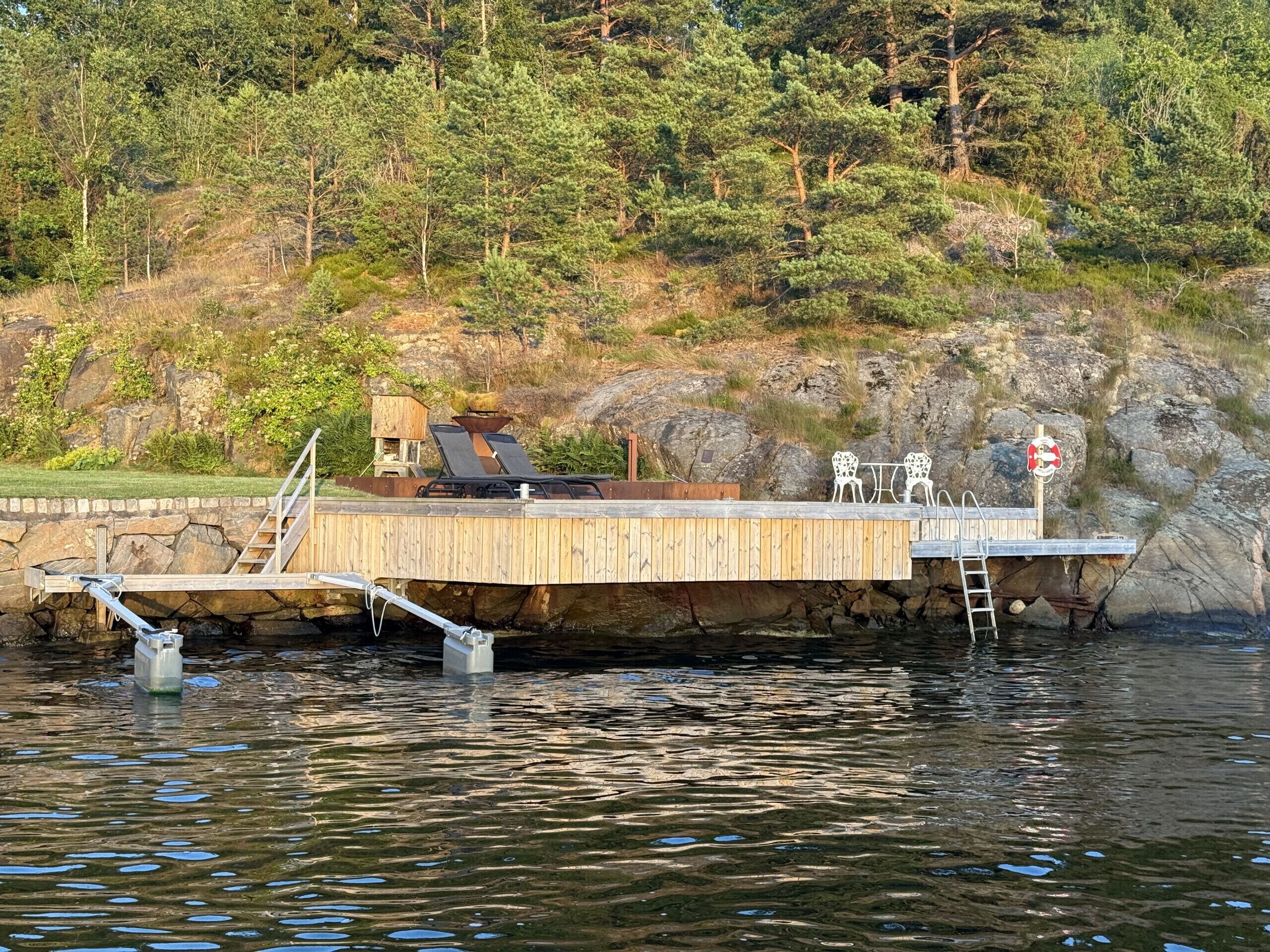 Une jetée s’avançant dans une étendue d’eau, avec une plateforme en bois, une petite construction dotée d’une cheminée et un panneau indiquant la présence d’une bouée de sauvetage.