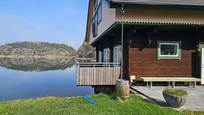 Eine Holzhütte mit einer Terrasse, die auf einen stillen See und eine bewaldete Insel blickt.