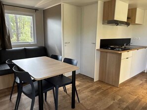 Una cocina compacta con comedor, una ventana con cortinas y vistas a árboles.