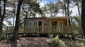 A wooden cabin with a deck, surrounded by trees.