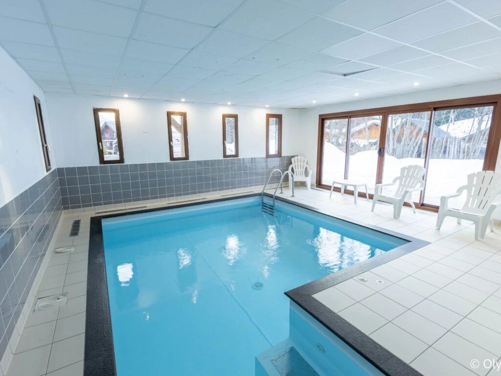Ein hallenbad mit großen Glaswänden, weißen Fliesenböden und einigen weißen Stühlen in der Nähe des Beckens.
