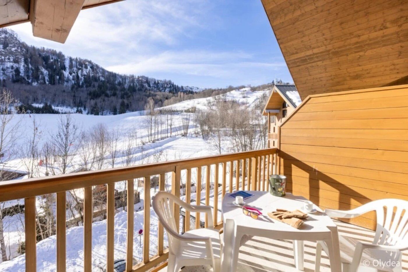 Une terrasse en bois avec une table et des chaises, d’où l’on peut admirer un paysage enneigé avec une montagne en arrière-plan.