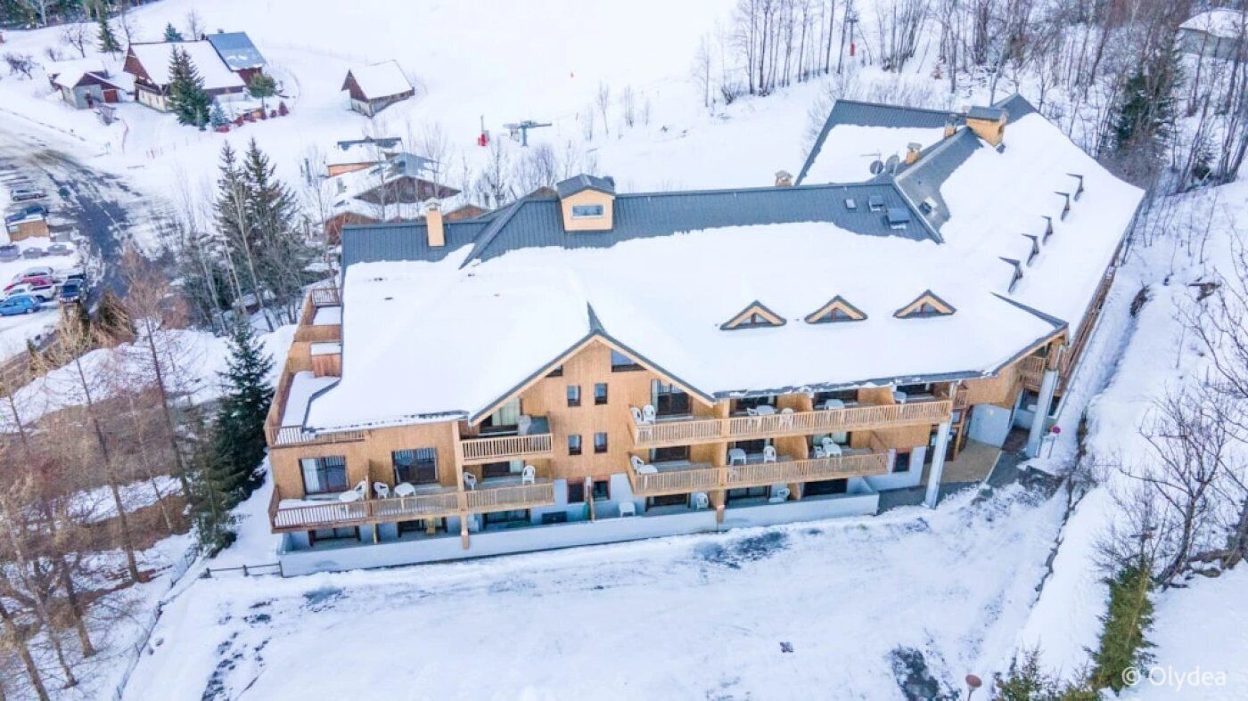 A large, multi-story building with a snow-covered roof, surrounded by trees and other buildings.