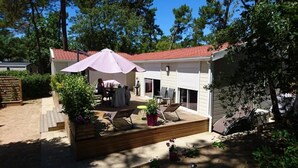 A covered patio with outdoor furniture, a wooden deck, and a red-tiled roof. - ZEcamping 4 étoiles locatif TV LV clim 88m2 (Saint-Hilaire-de-Riez)