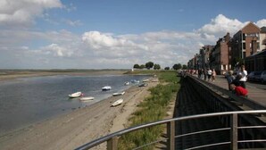 Un paseo a orillas del río con barcos, una playa de arena y edificios a lo largo de la ribera.