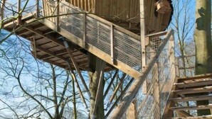 Una torre de madera con suelo de malla metálica, rodeada por una cerca de madera.