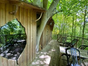 Una terraza de madera con mesas y sillas, rodeada de árboles.