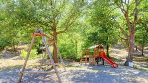 Ein Spielplatz mit Schaukel und Rutsche, umgeben von Bäumen und Kies.