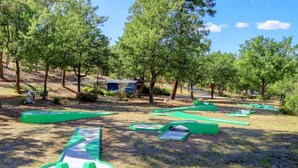Ein Spielbereich im Freien mit grünen Rutschen und Klettergerüsten, umgeben von Bäumen.