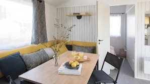 Ein modernes, kompaktes Wohnzimmer mit Essbereich, einer Couch mit gemusterten Kissen, einem kleinen Tisch mit Vase und Zitronenschale sowie einem Bücherregal.