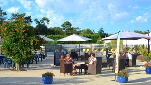 An outdoor seating area with tables and chairs, surrounded by potted plants and umbrellas.