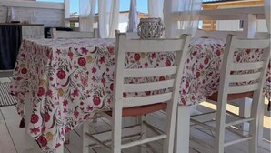 An outdoor dining area with a table covered in a floral tablecloth, white chairs, and a hanging light fixture.