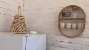 A kitchen with a white refrigerator, a woven sugar container, and a round shelf with white mugs and a small basket.