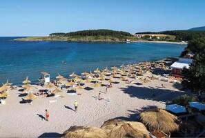 A beach with numerous sun umbrellas and beach chairs, a clear blue sea, and a small hill in the background. - Каравана с просторна веранда, собствена баня и кухня! (Arapya, Tsarevo)