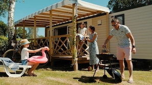 Eine Familie grillt draußen unter einer hölzernen Pergola, im Hintergrund ein Wohnmobil.