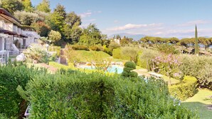 A lush garden with a swimming pool, stone pathway, and a view of a hillside with trees and a distant mountain. - Horizon luxury lake view by Bookinggardalake (Moniga del Garda)