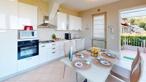 A modern kitchen with white cabinets, a microwave, stove, and oven. There is a dining table set with plates and a vase of flowers. - Horizon luxury lake view by Bookinggardalake (Moniga del Garda)