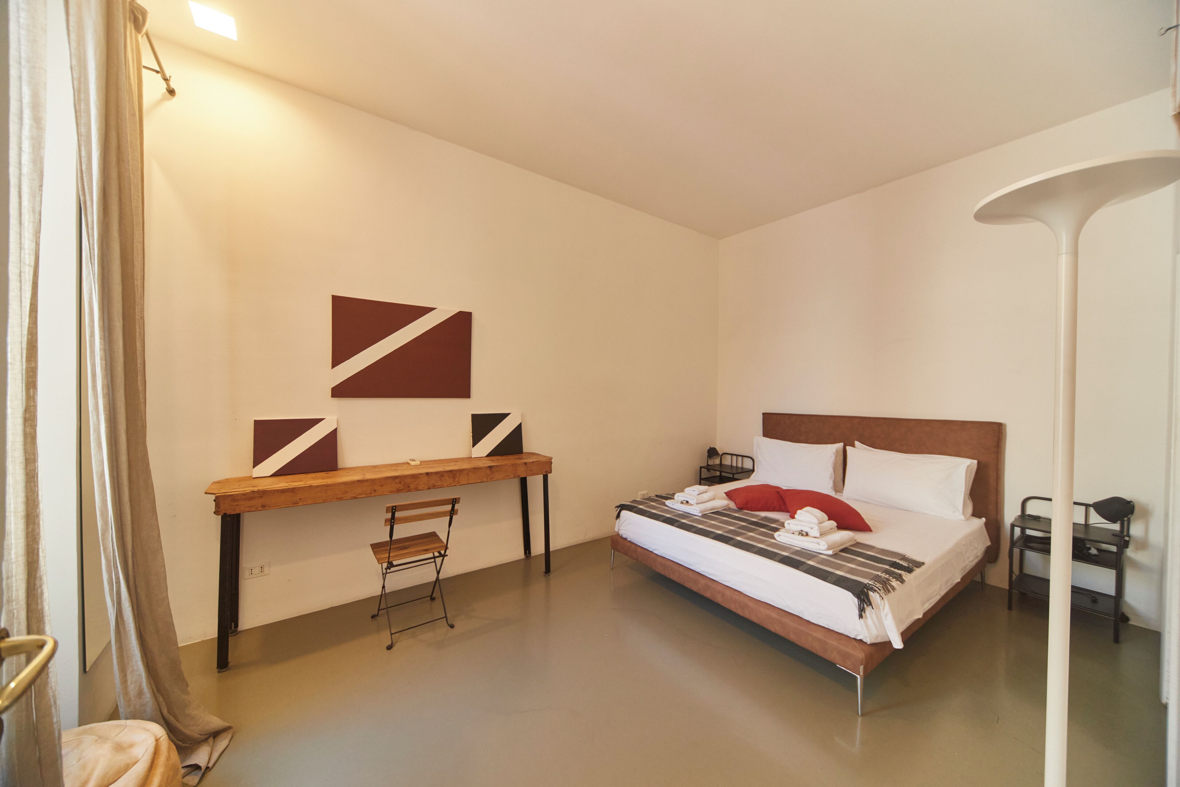 Une chambre à coucher avec un lit, un bureau, une chaise et une lampe sur pied.
