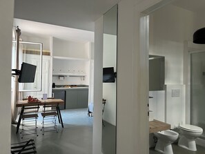 Moderni keittiö, jossa on valkoiset kaapit, ruokailutila pöydän ja tuolien kera sekä kylpyhuone, jossa on wc ja bidee.